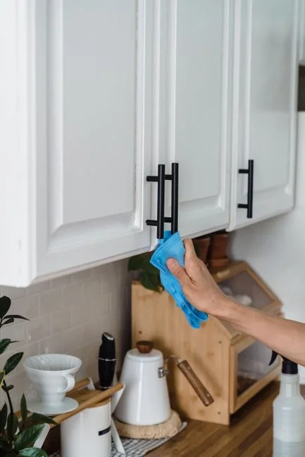 Close-up of hand cleaning window with squeegee outdoors using yellow gloves.